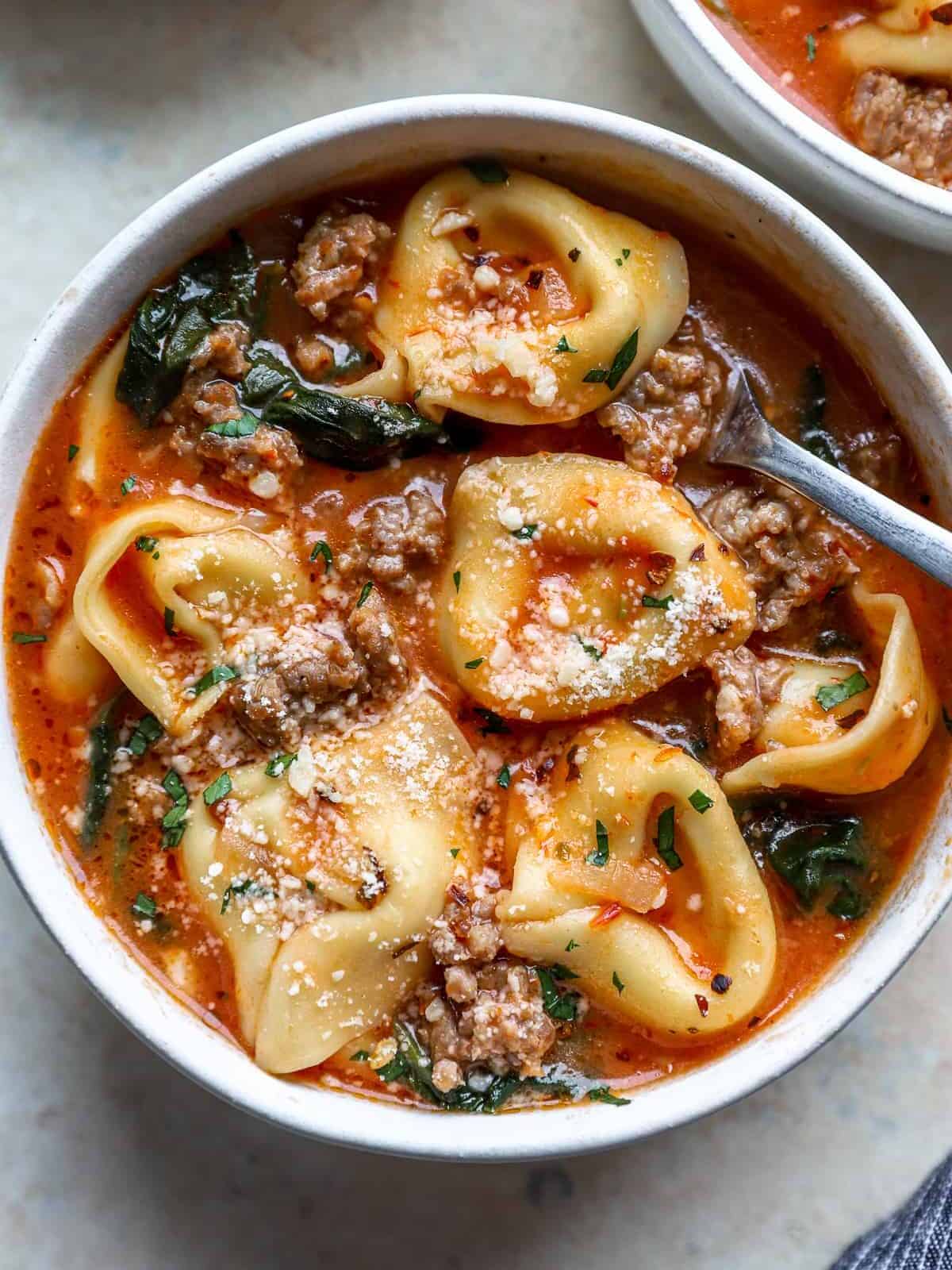 overhead view of tortellini soup in a white bowl with a spoon.