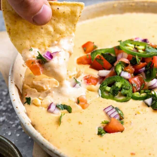 a hand dopping a tortilla chips into a bowl of homemade white queso.