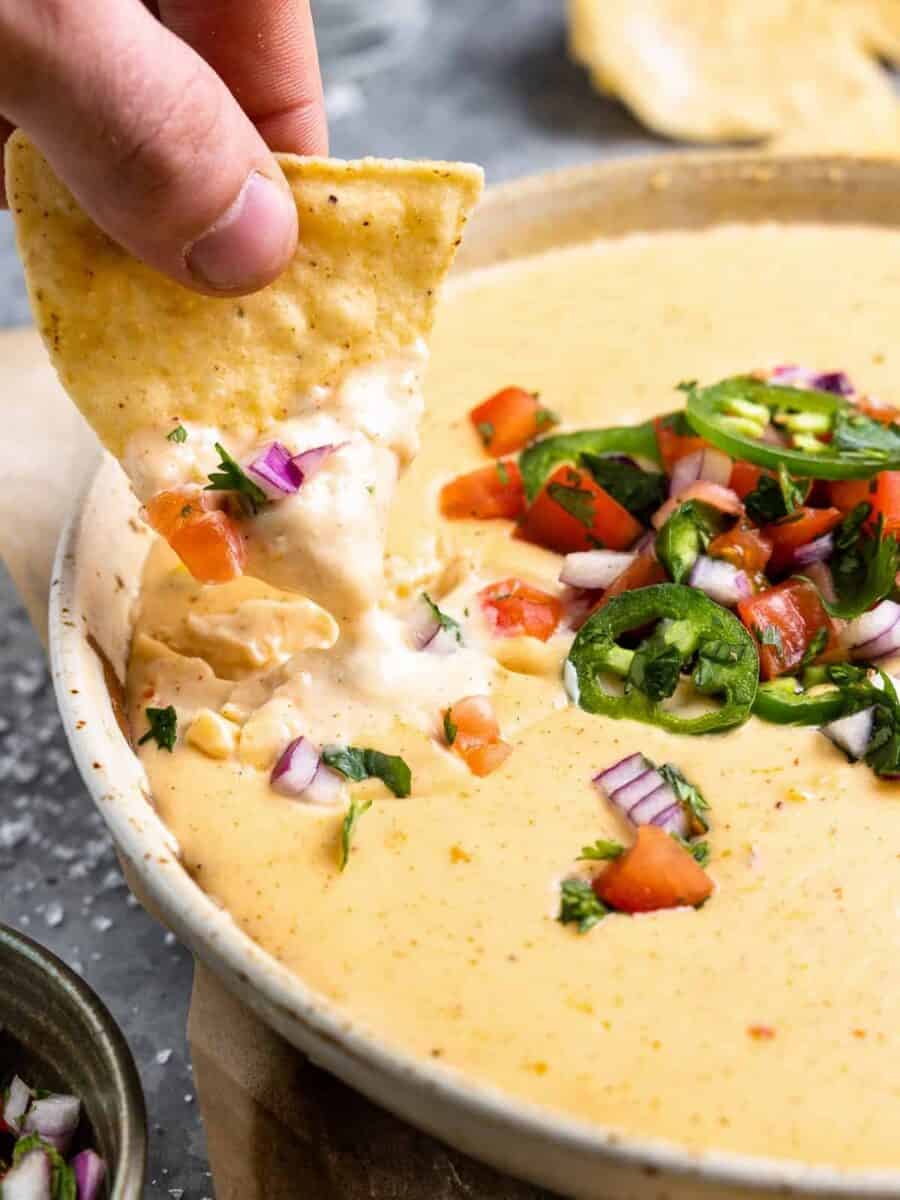 a hand dopping a tortilla chips into a bowl of homemade white queso.