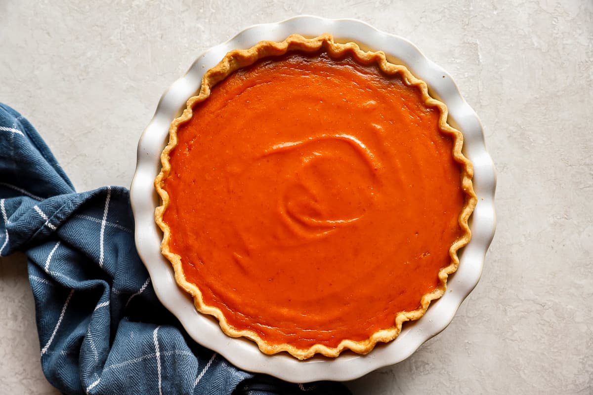 A pumpkin pie in a white dish on a table.