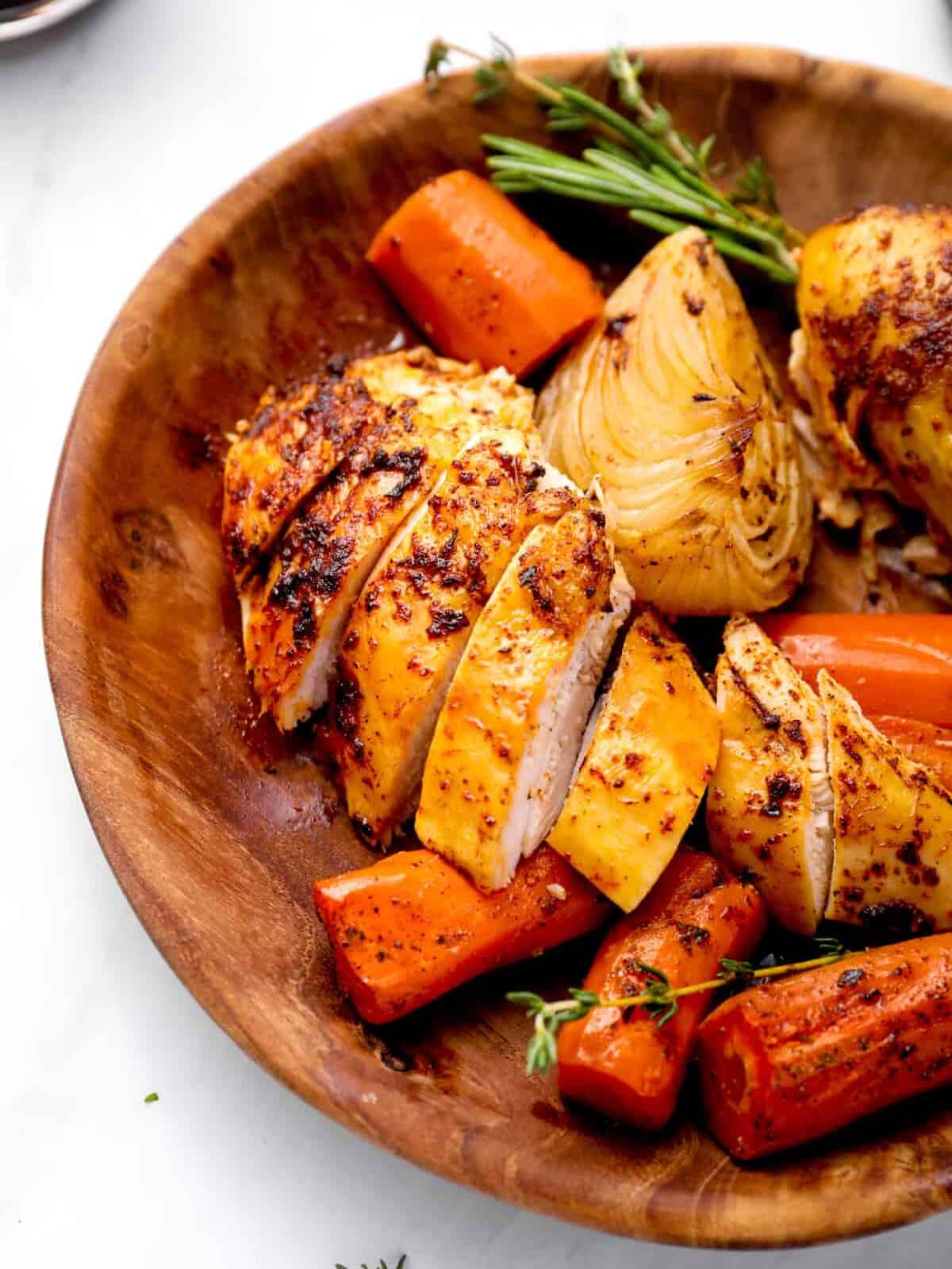 close up of sliced crockpot whole chicken in a wooden bowl with vegetables and herbs.