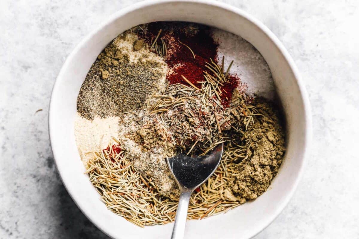 a spoon mixing turkey rub in a white bowl.