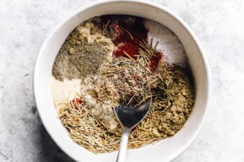 a spoon mixing turkey rub in a white bowl.