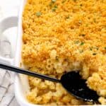 close up of mac and cheese casserole in a white baking pan with a black serving spoon.