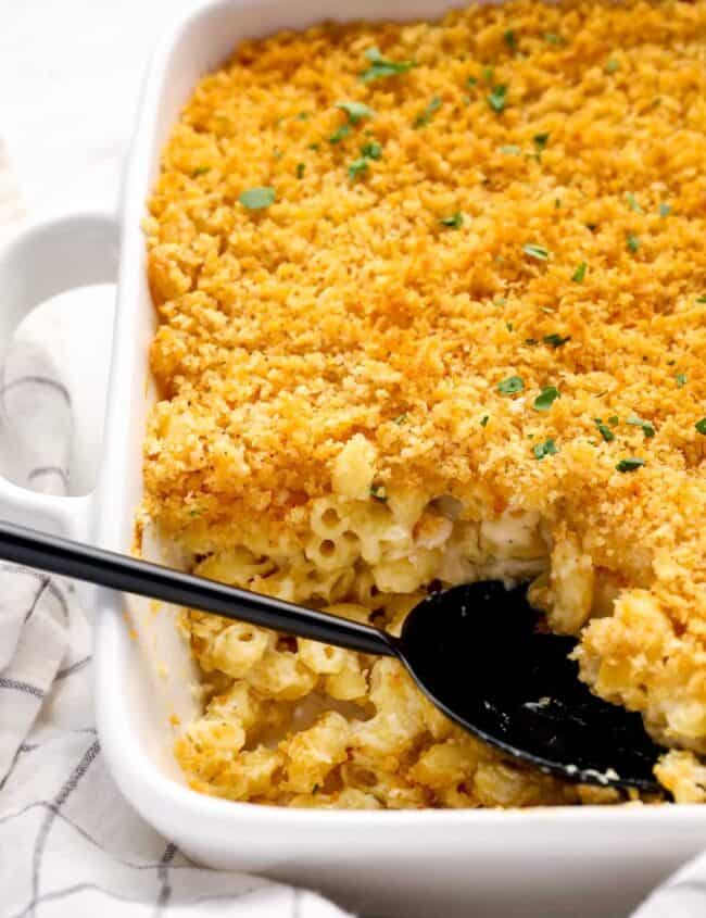 close up of mac and cheese casserole in a white baking pan with a black serving spoon.