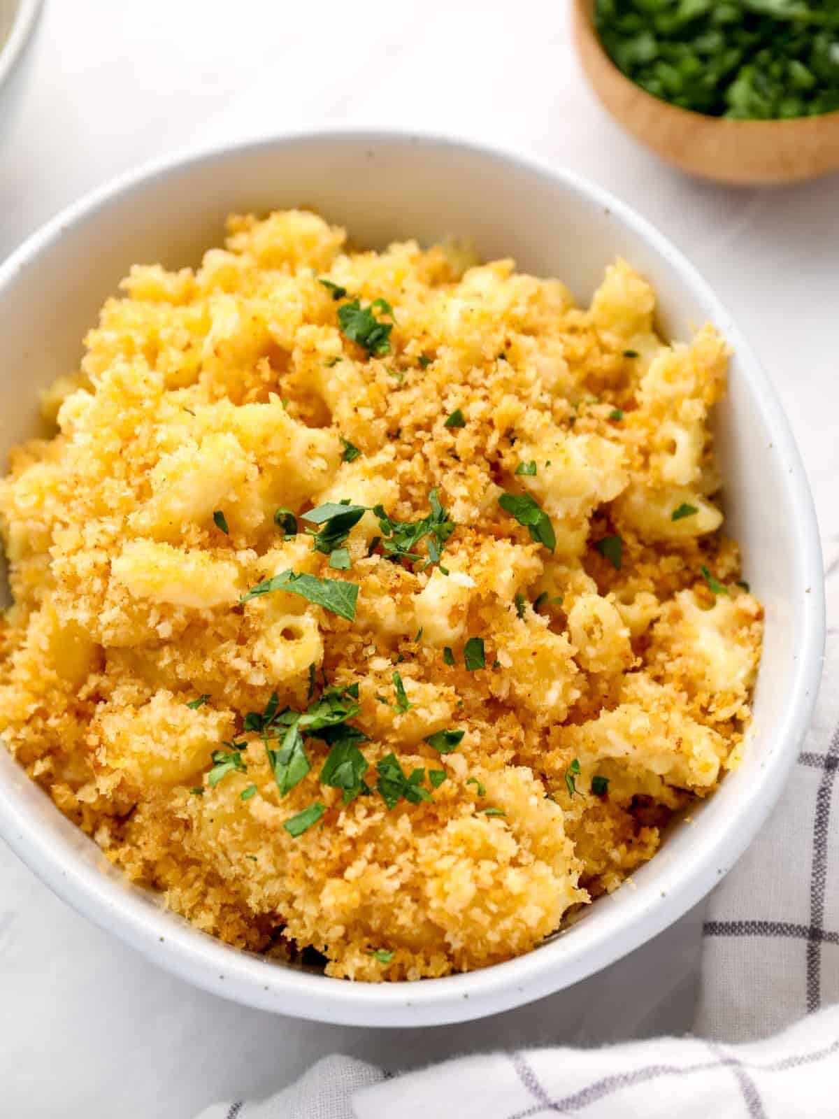 a serving of mac and cheese casserole in a white bowl with parsley.