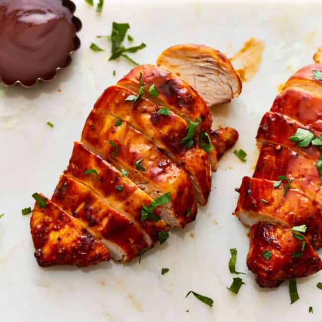 Two chicken breasts on a cutting board with sauce.