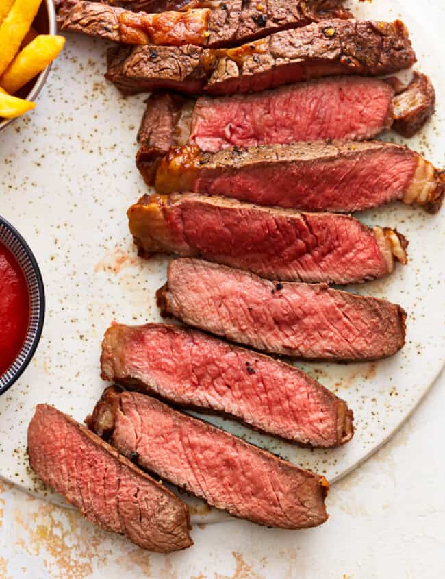 Steak with ketchup and fries on a white plate.