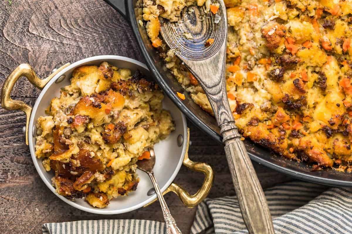 A pan of sausage stuffing and mashed potatoes with a spoon.