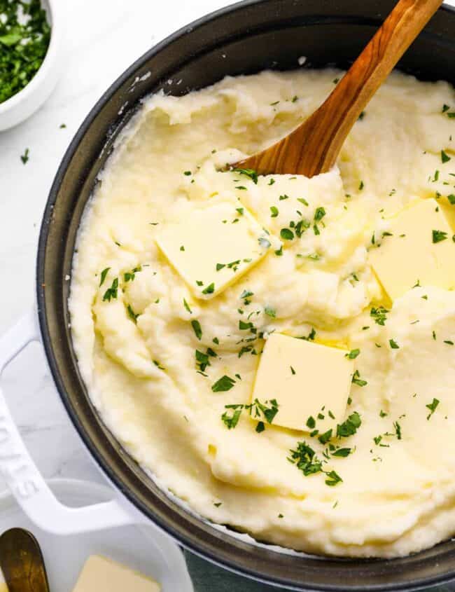 creamy mashed potatoes in a cast iron skillet with a wooden spoon.