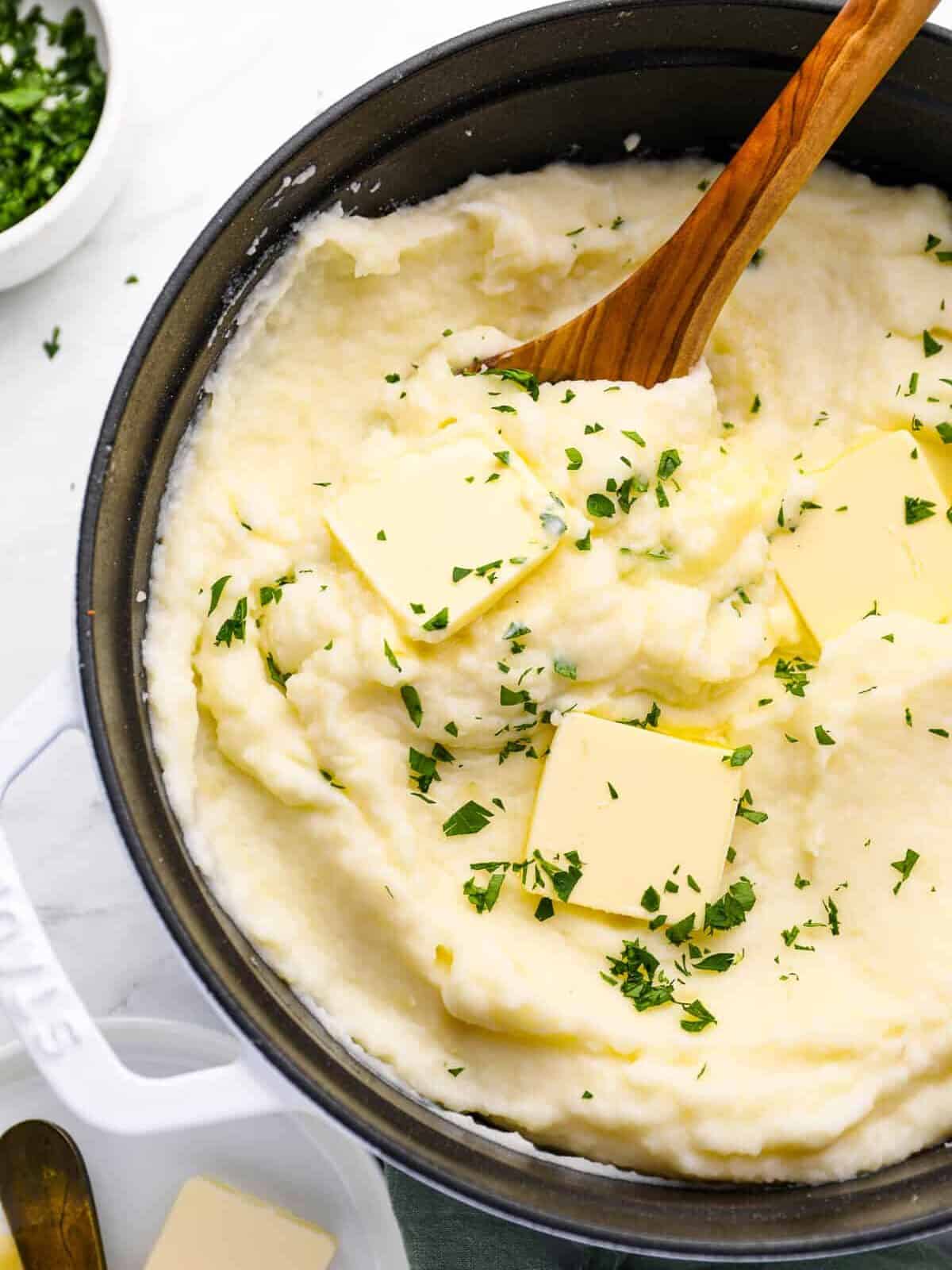 mashed potatoes in a cast iron skillet with a wooden spoon.