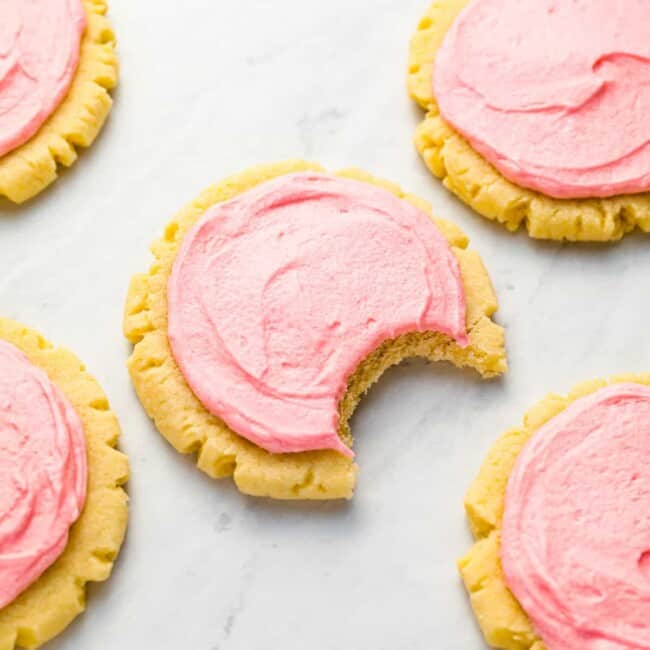 Pink frosted cookies with a bite taken out of them.