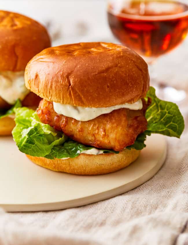 Two fish burgers on a plate next to a glass of beer.