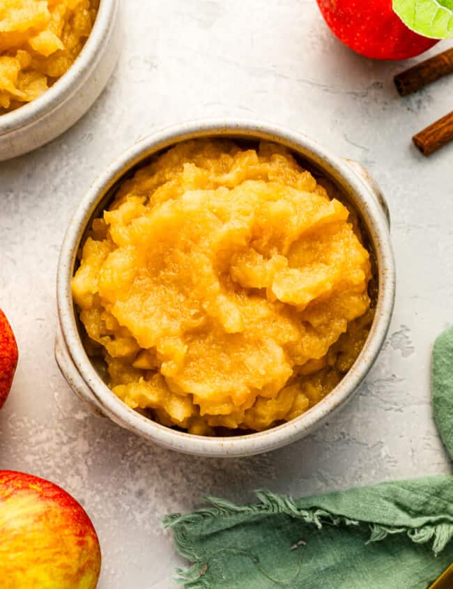 A bowl of applesauce with cinnamon sticks and apples.