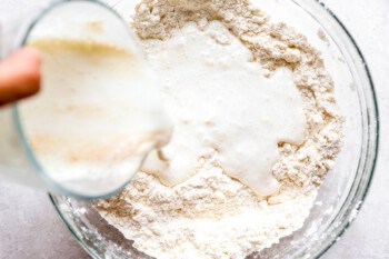 A person pouring milk into a bowl of flour.