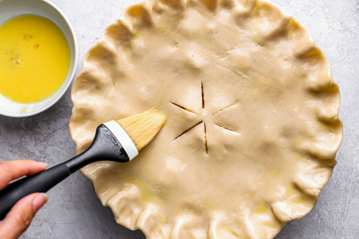 A person is using a brush to make a pie crust.