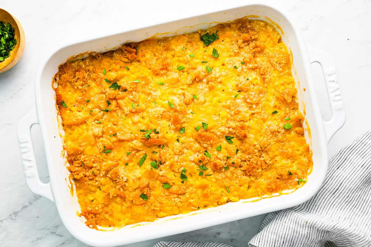 baked scalloped corn casserole in a white baking dish.