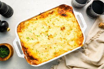 A white dish with a casserole on it next to a bottle of wine.