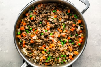 A skillet full of ground beef, carrots and peas.