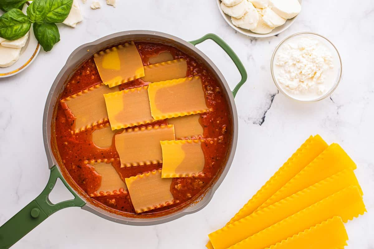 Broken lasagna noodles arranged on top of meat sauce in a skillet.