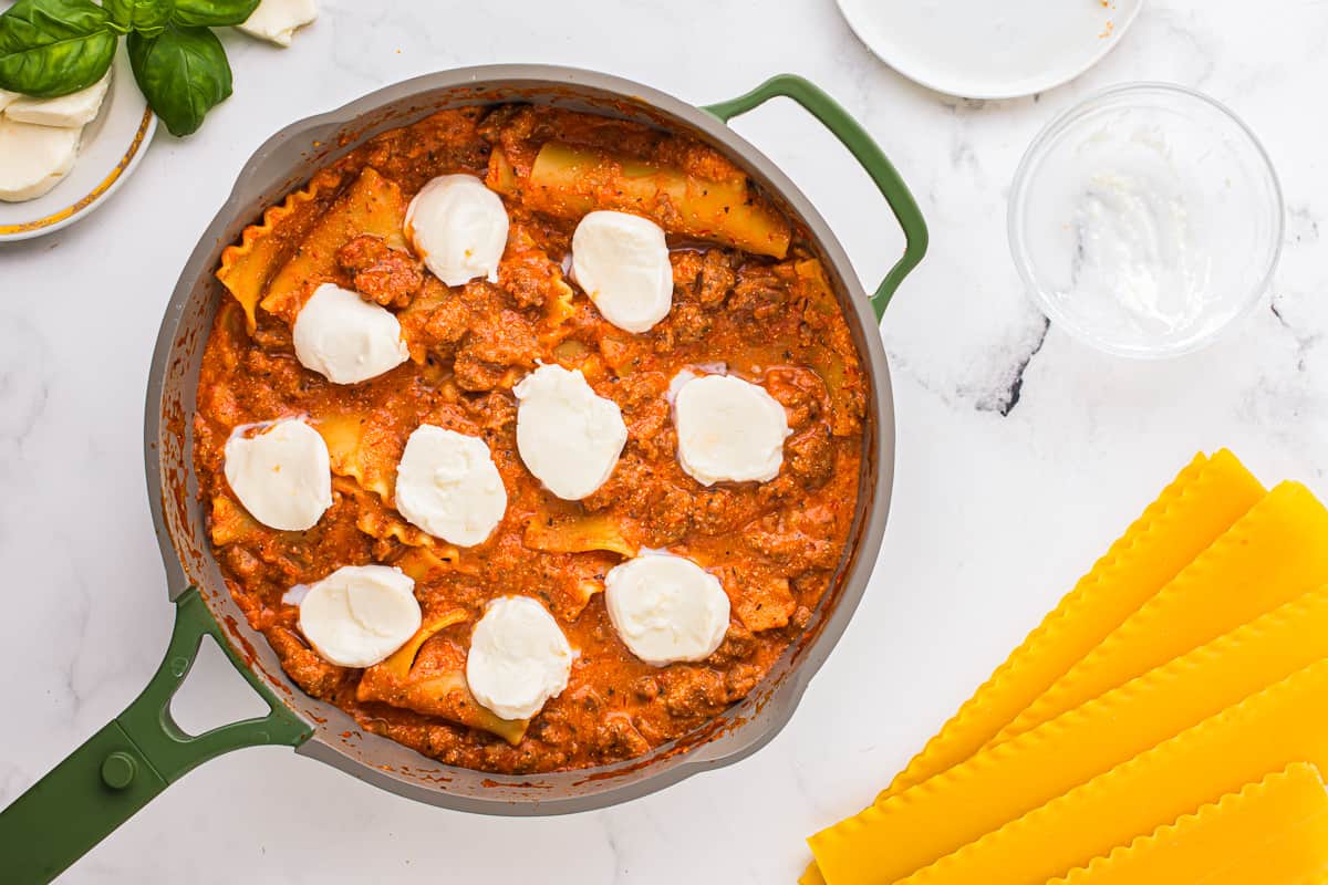 Lasagna in a pan, topped with slices of mozzarella.