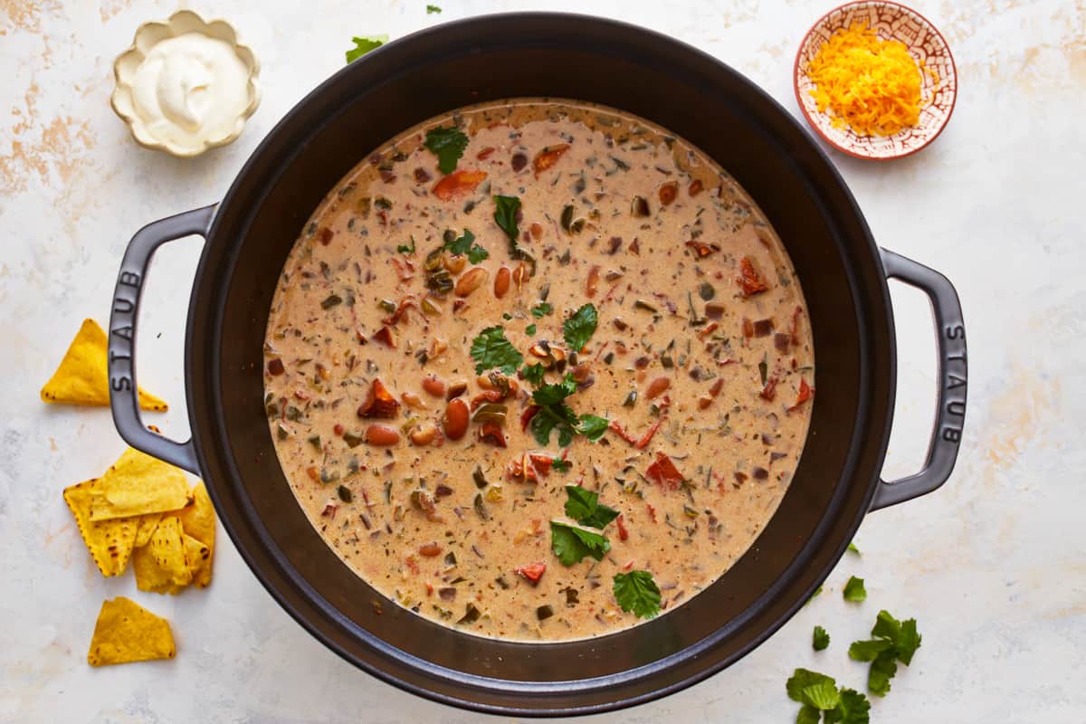 A pot of white chicken chili with tortilla chips and salsa.