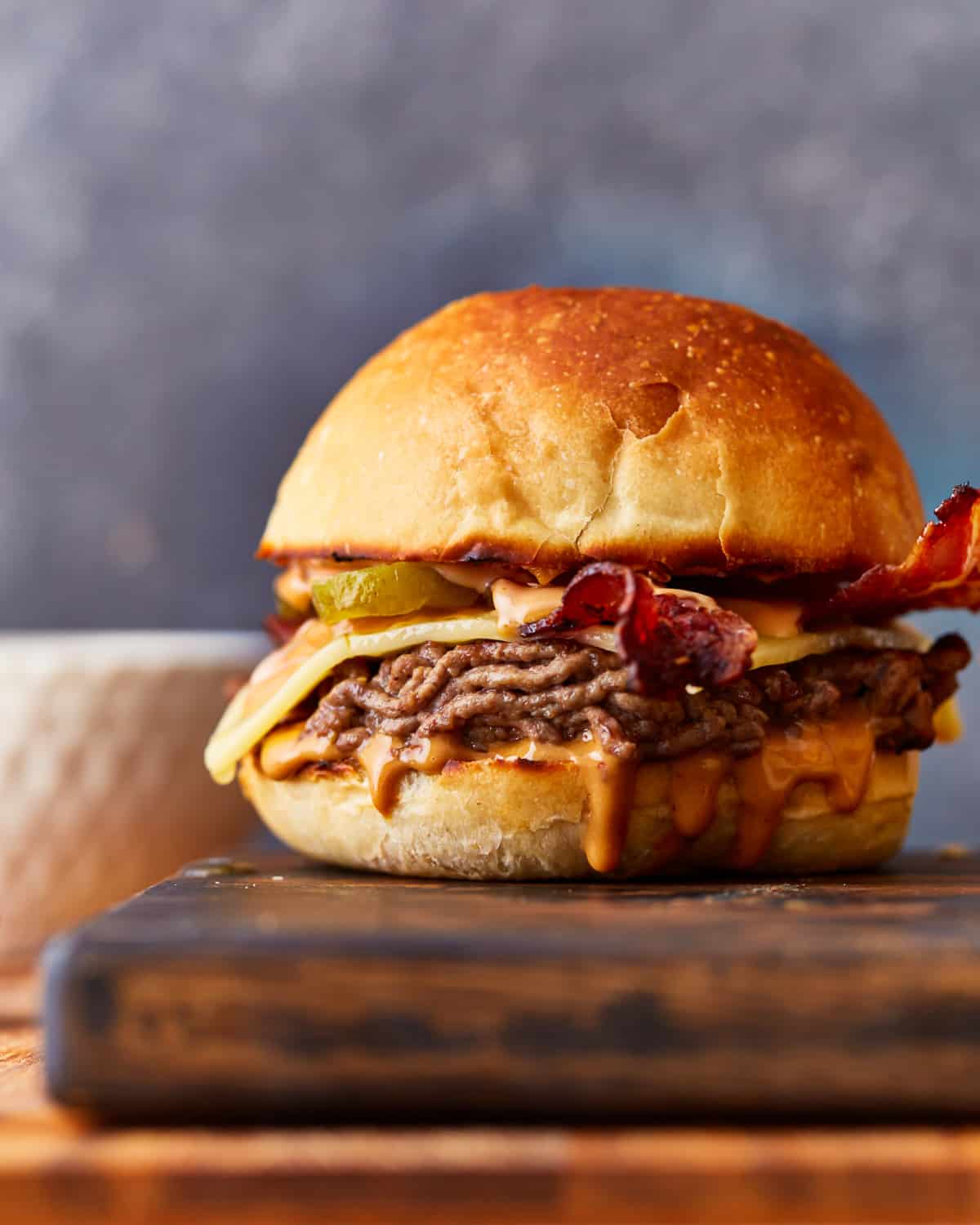 A burger with bacon and cheese on a cutting board.