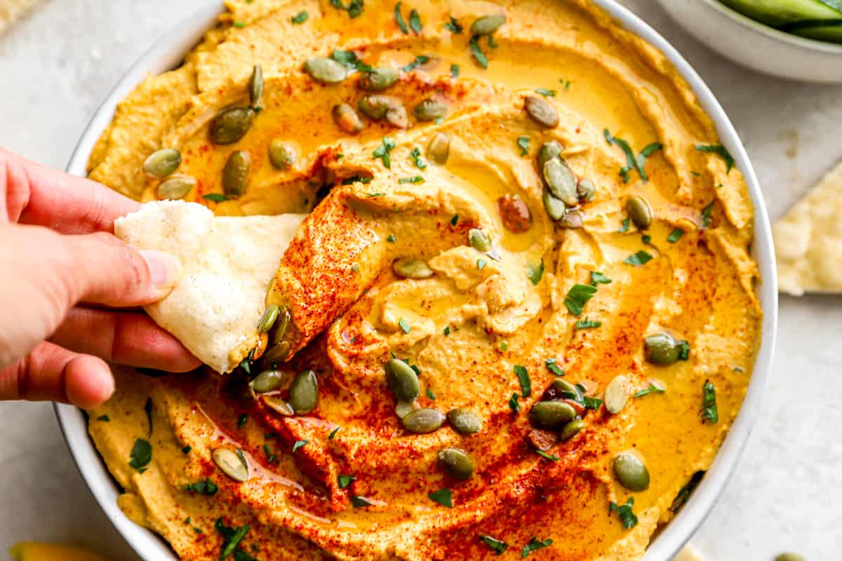 A person dipping a cracker into a bowl of pumpkin hummus.