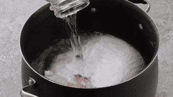 pouring water over a raw turkey breast in a bath of brine.