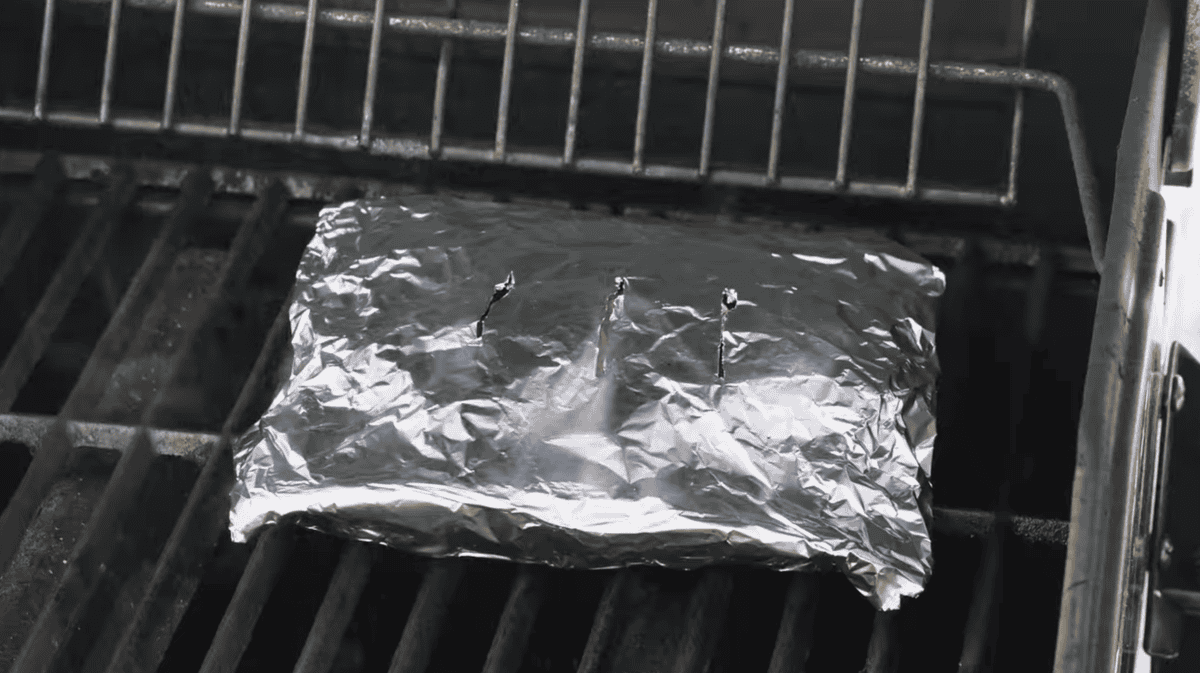 a smoking foil packet of wood chips on a grill.