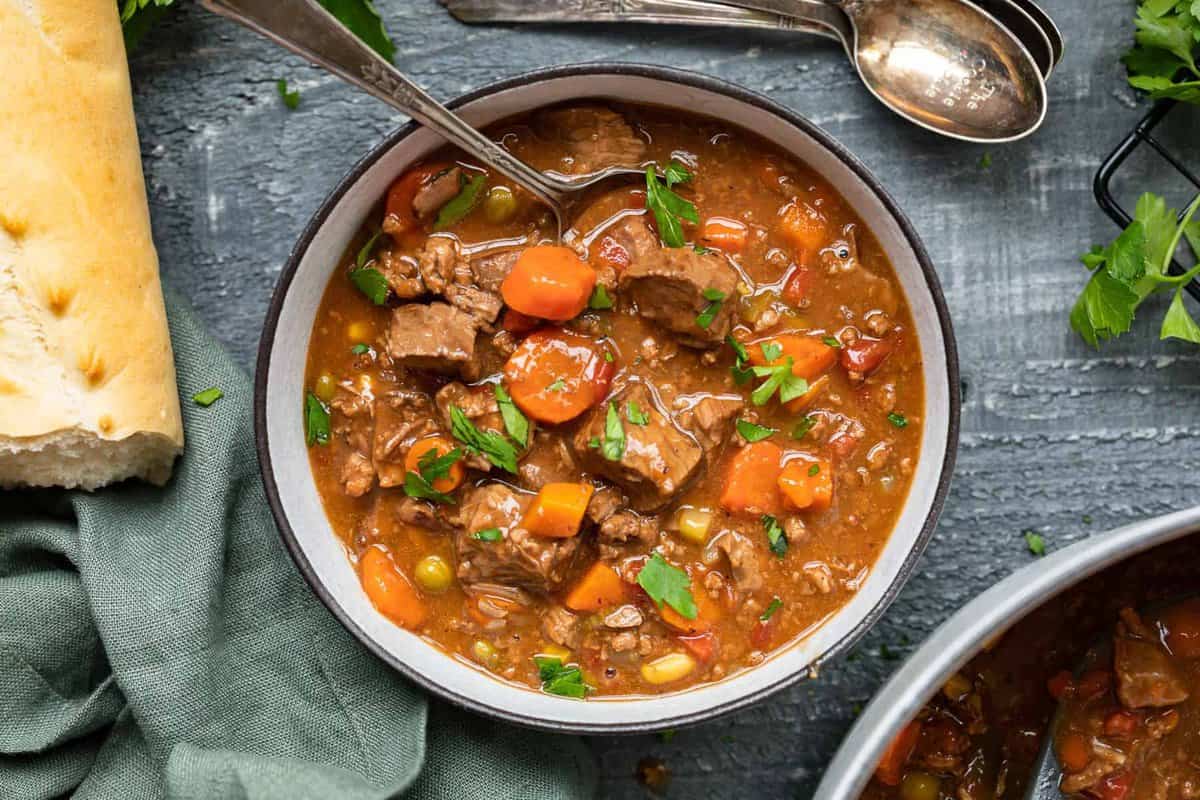 overhead view of a serving of steak soup in a white bowl with a spoon.