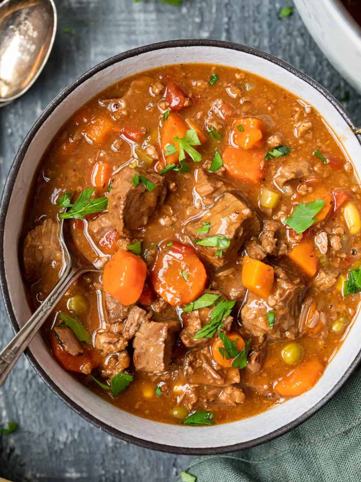 close-up overhead view of a serving of steak soup in a white bowl with a spoon.