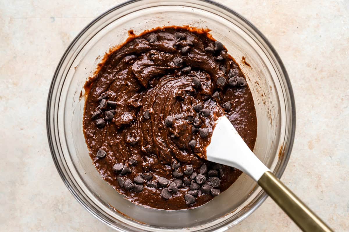 brownie batter with chocolate chips in a glass bowl with a rubber spatula.