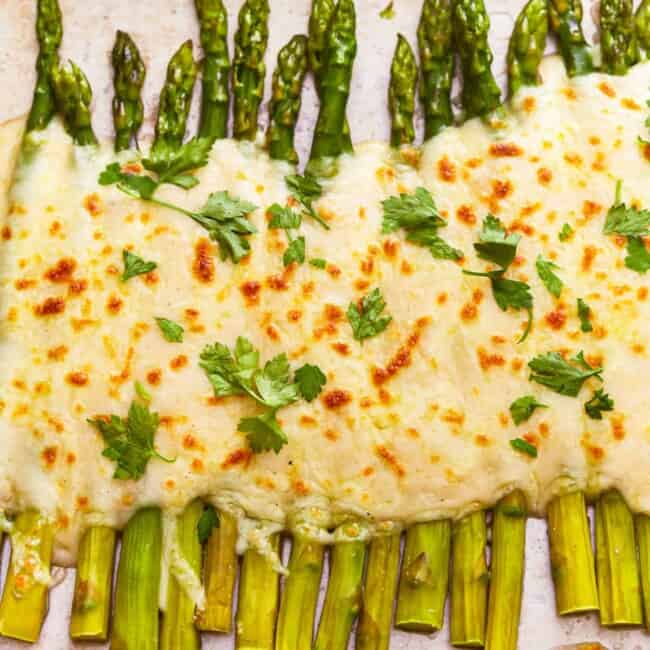 A tray of asparagus gratin topped with cheese and parsley.