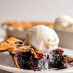 A slice of blueberry pie with ice cream on a plate.