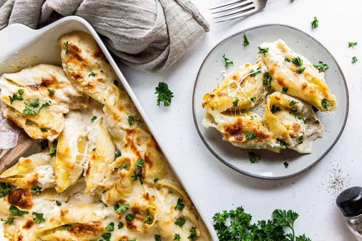 pasta shells stuffed with cheese and chicken topped with alfredo sauce on a white plate