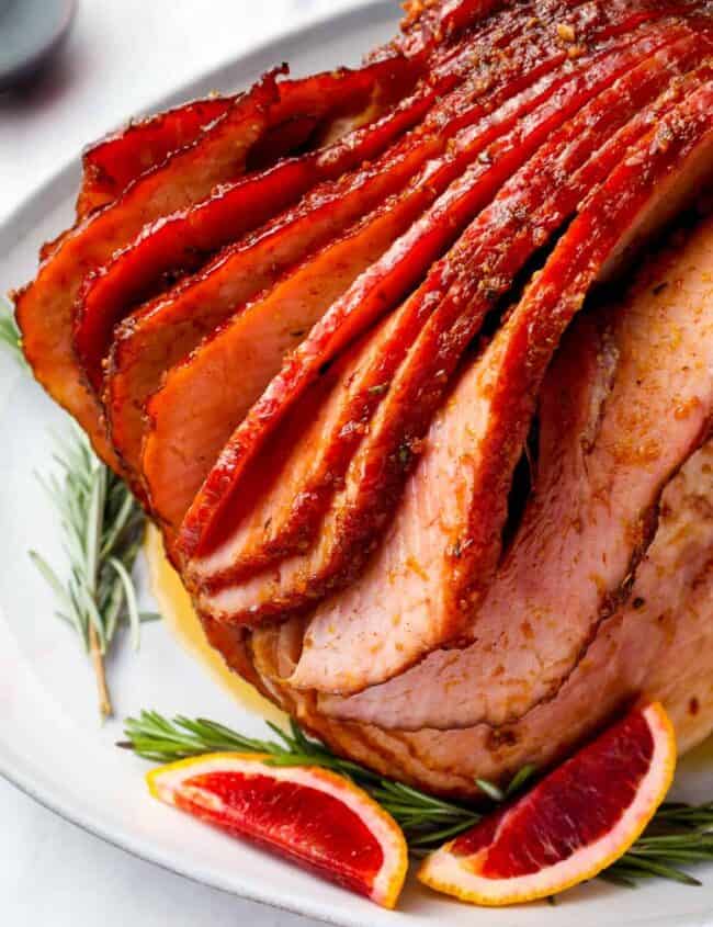 sliced ham with blood oranges and rosemary on a white plate.