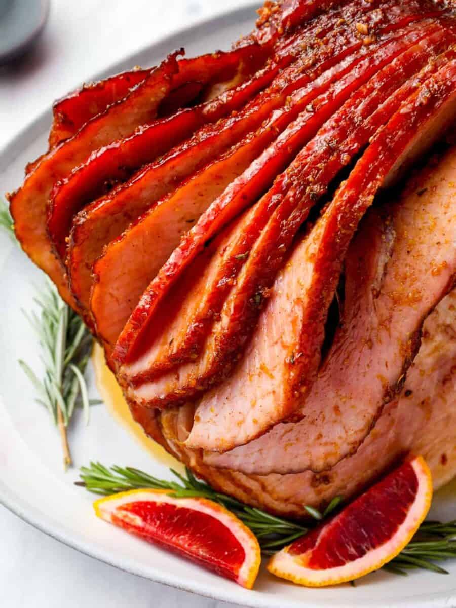 sliced ham with blood oranges and rosemary on a white plate.