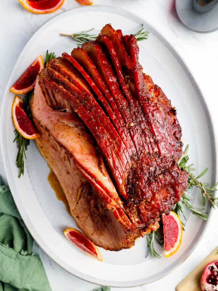 a roasted ham with blood oranges on a plate.