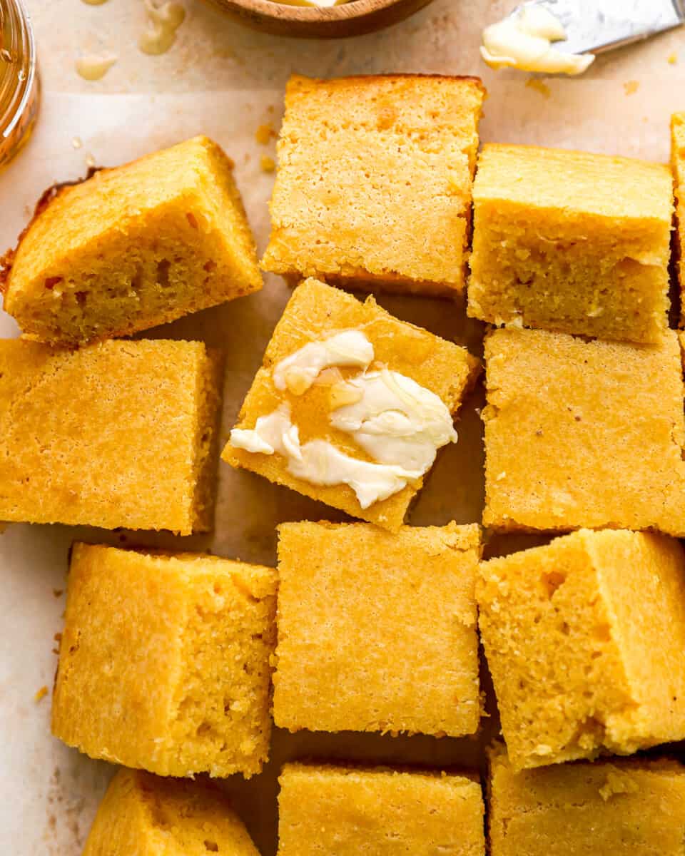 Cornbread squares with butter and honey on a baking sheet.