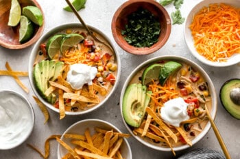 bowls of creamy chicken tortilla soup topped with avocado, tortilla strips, cheese, and sour cream.