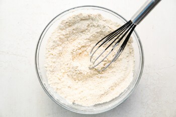 A bowl of flour with a whisk in it.