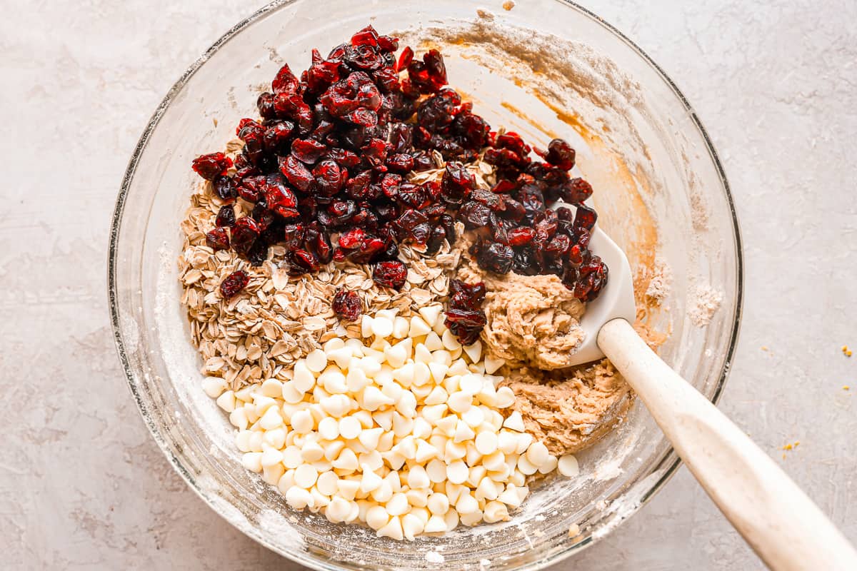 Cookie dough in a bowl with cranberries, oats, and white chocolate chips.