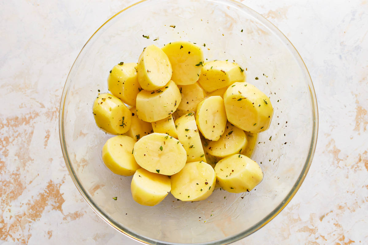 Sliced potatoes in a glass bowl with herbs.