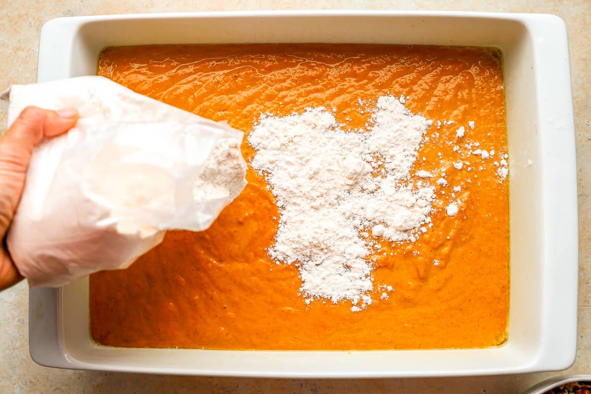 A person pouring cake mix over a pan filled with cake batter.