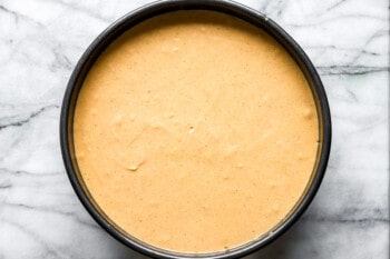 A bowl filled with a yellow batter on a marble countertop.