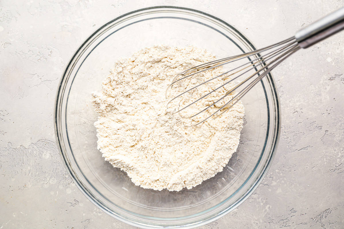 A bowl of flour with a whisk in it.