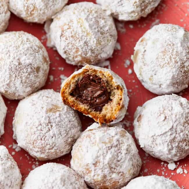 A plate of stuffed snowball cookies with a bite taken out of them.