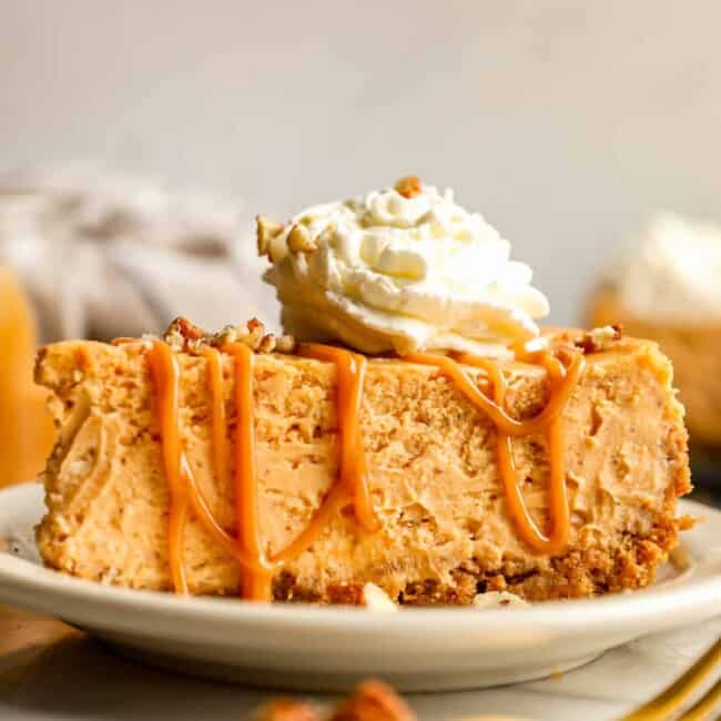 A slice of pumpkin cheesecake on a plate with whipped cream and pecans.