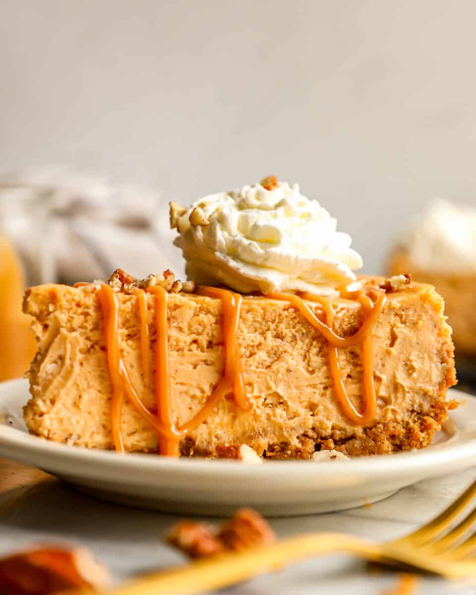 A slice of sweet potato cheesecake on a plate with whipped cream and pecans.